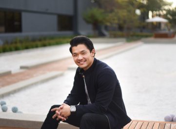 Han Jin sitting on bench smiling into the camera